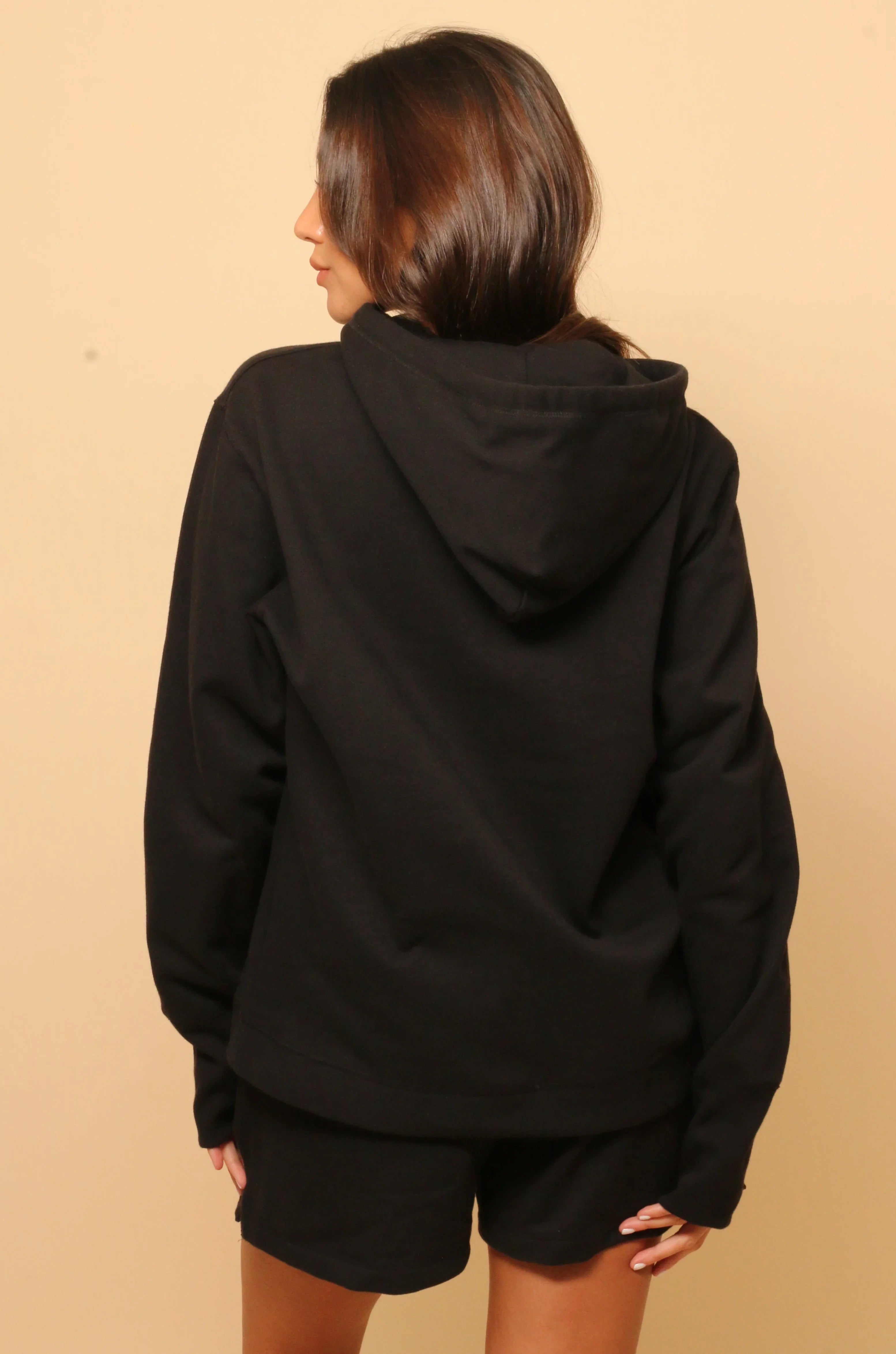 Back view of woman wearing black hypoallergenic cotton hoodie and shorts against beige background