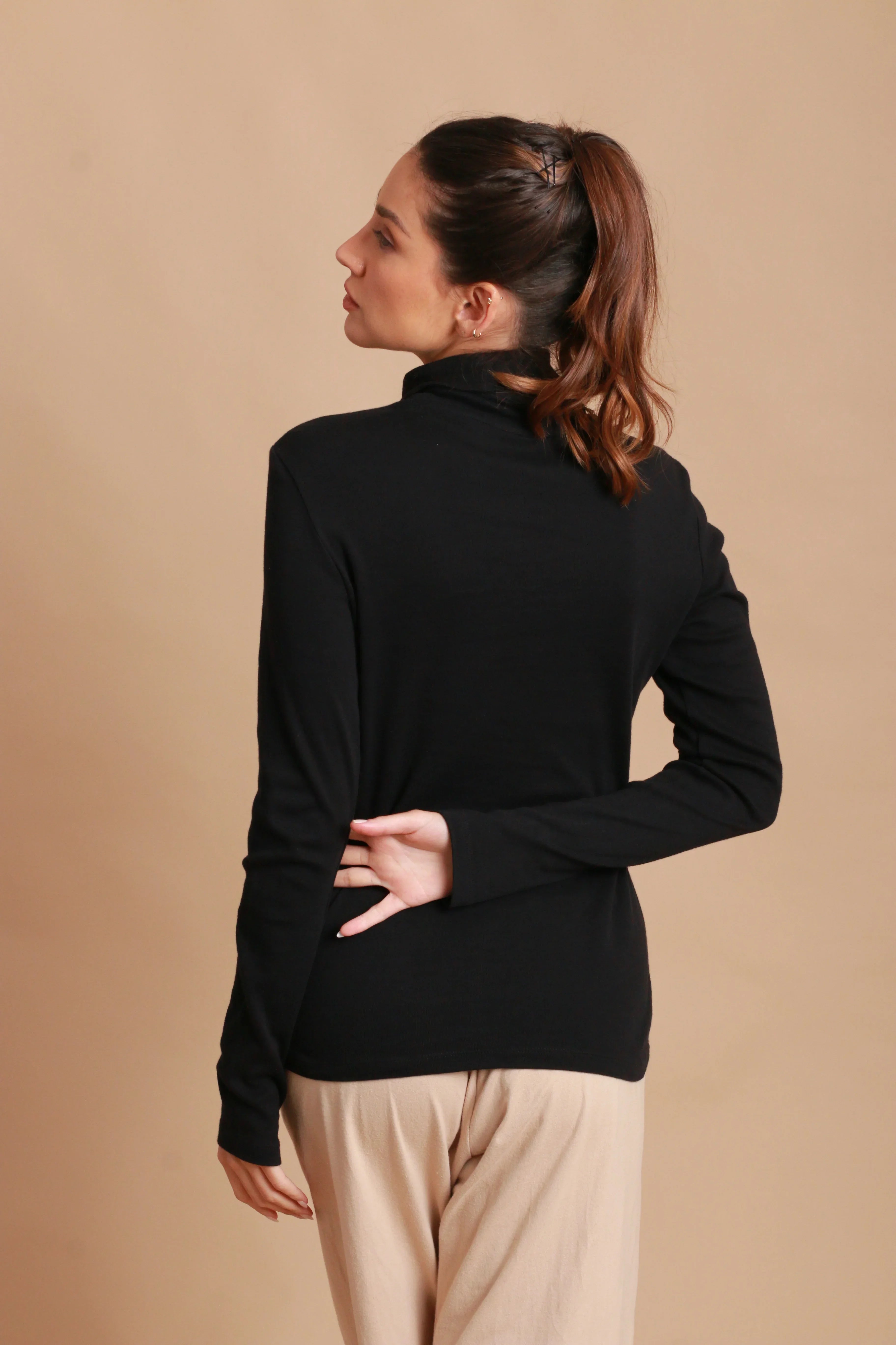 Woman wearing black allergy-free Cottonique long-sleeve top and beige pants, back view