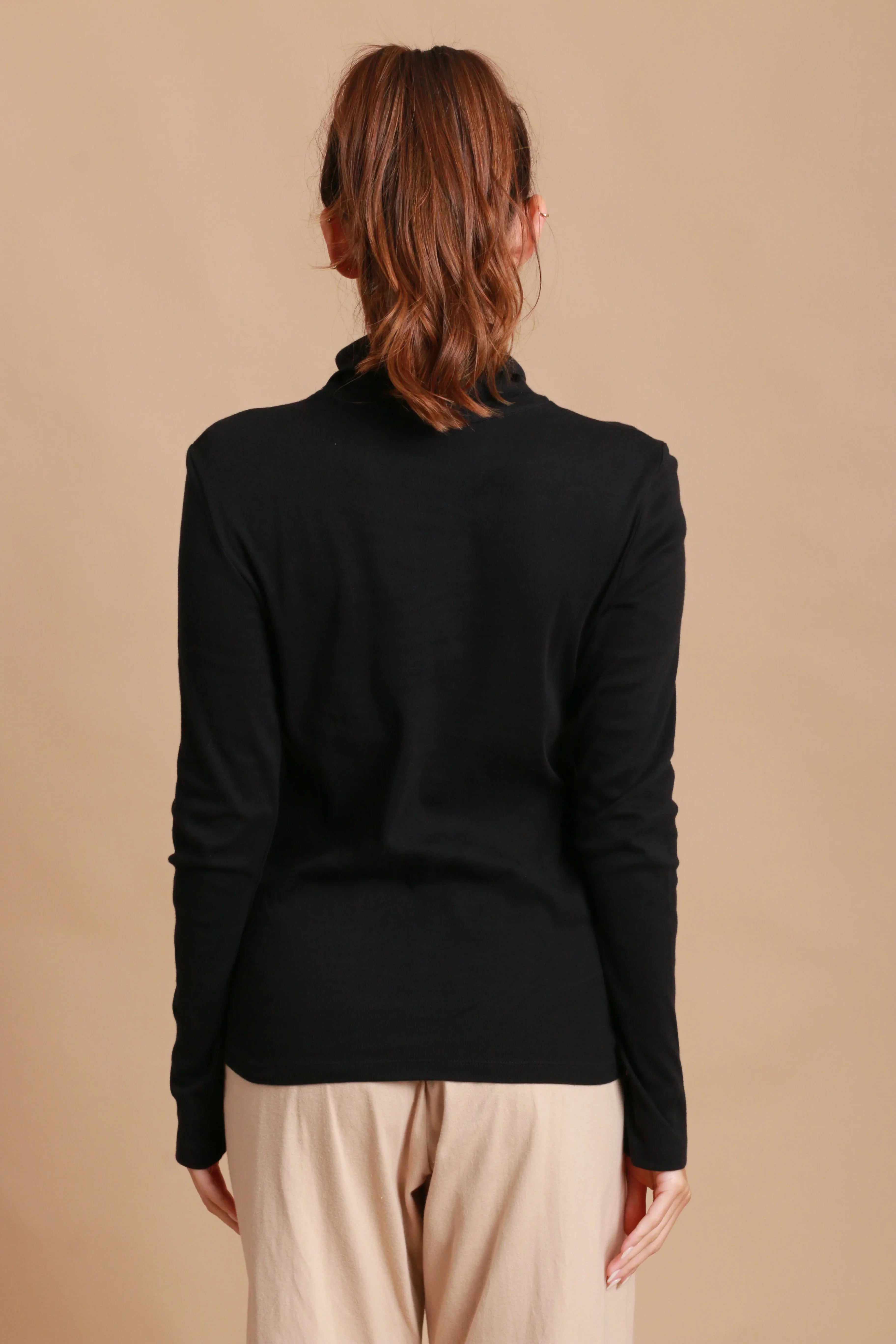 Woman wearing black hypoallergenic long-sleeve top and beige pants, back view