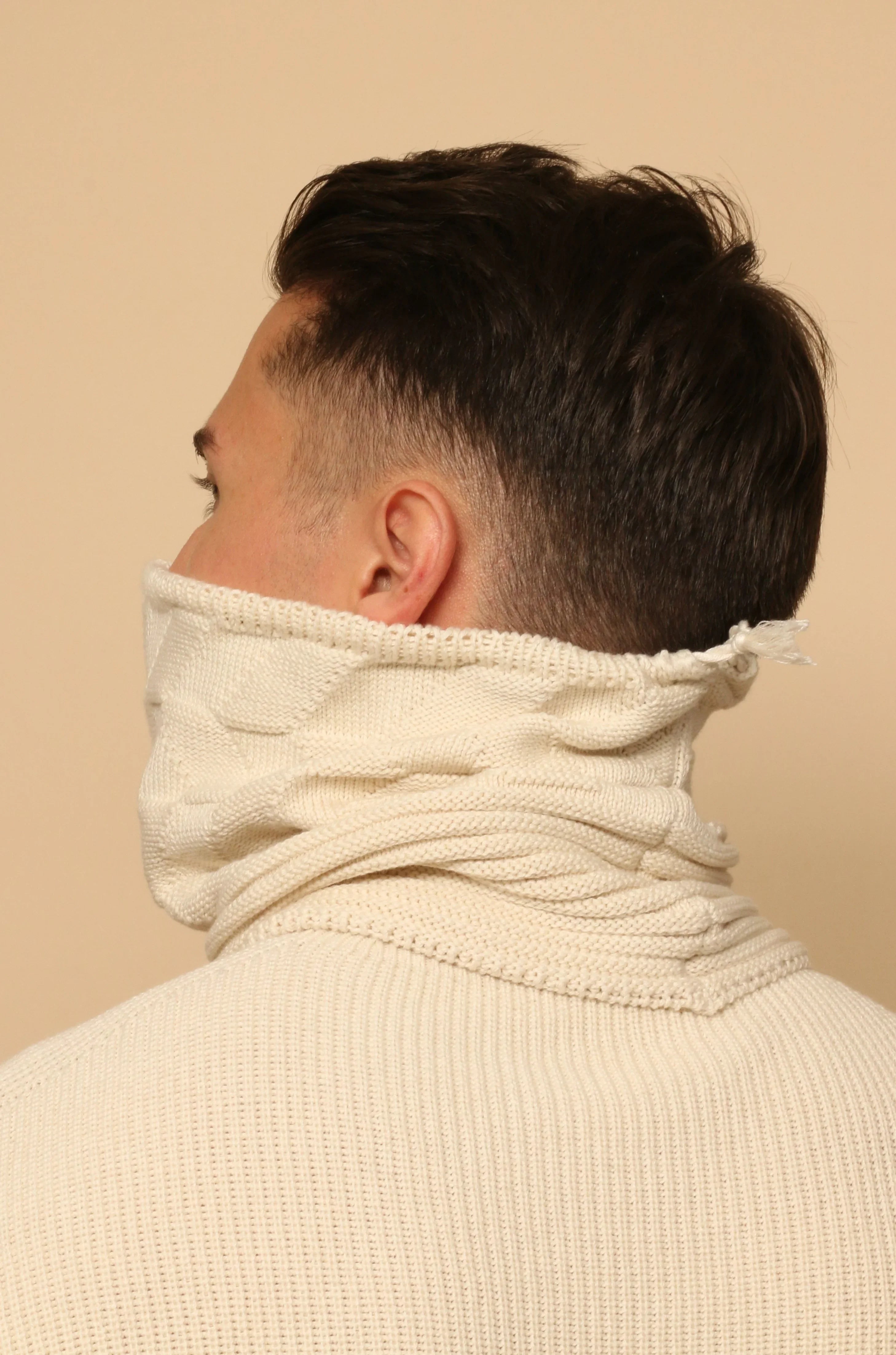 Back view of a man wearing a cream organic cotton knit neck gaiter and sweater