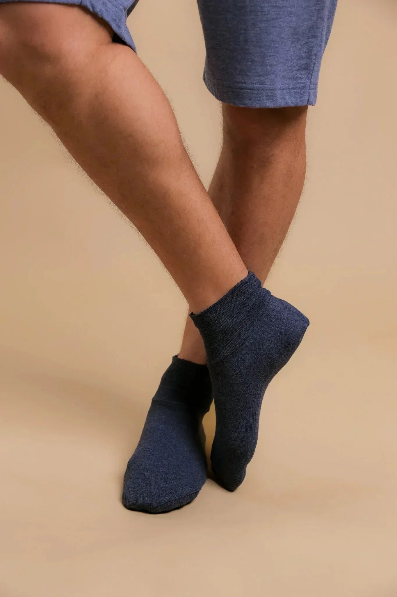 Man wearing blue hypoallergenic cotton ankle socks and shorts against beige background
