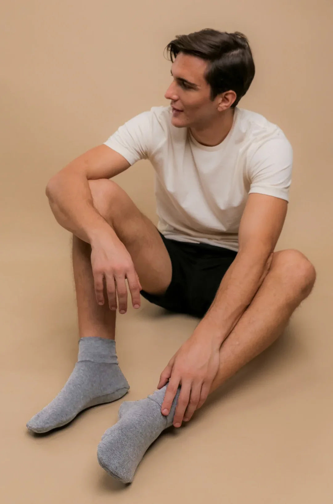 Man wearing organic cotton t-shirt, shorts, and gray allergy-free socks sitting on floor