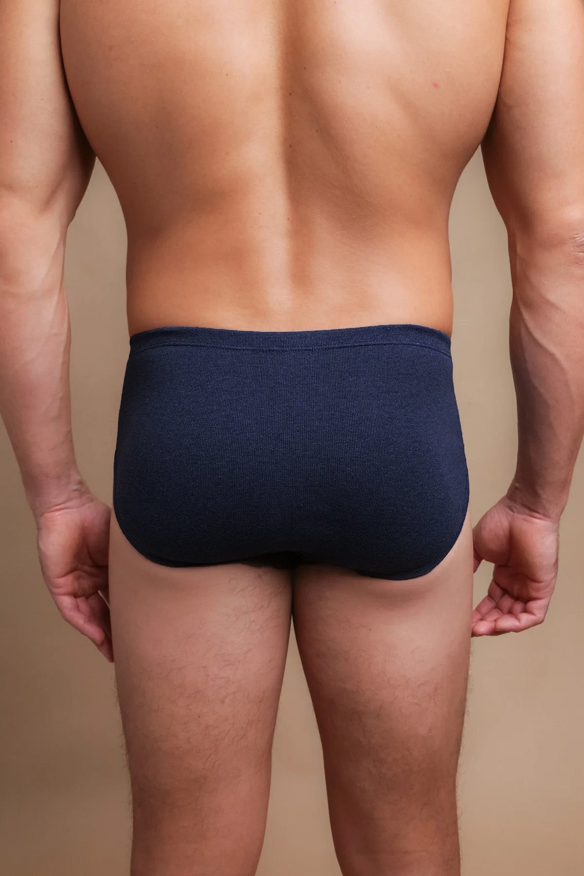 Back view of a man wearing navy blue hypoallergenic Cottonique underwear against a tan background.