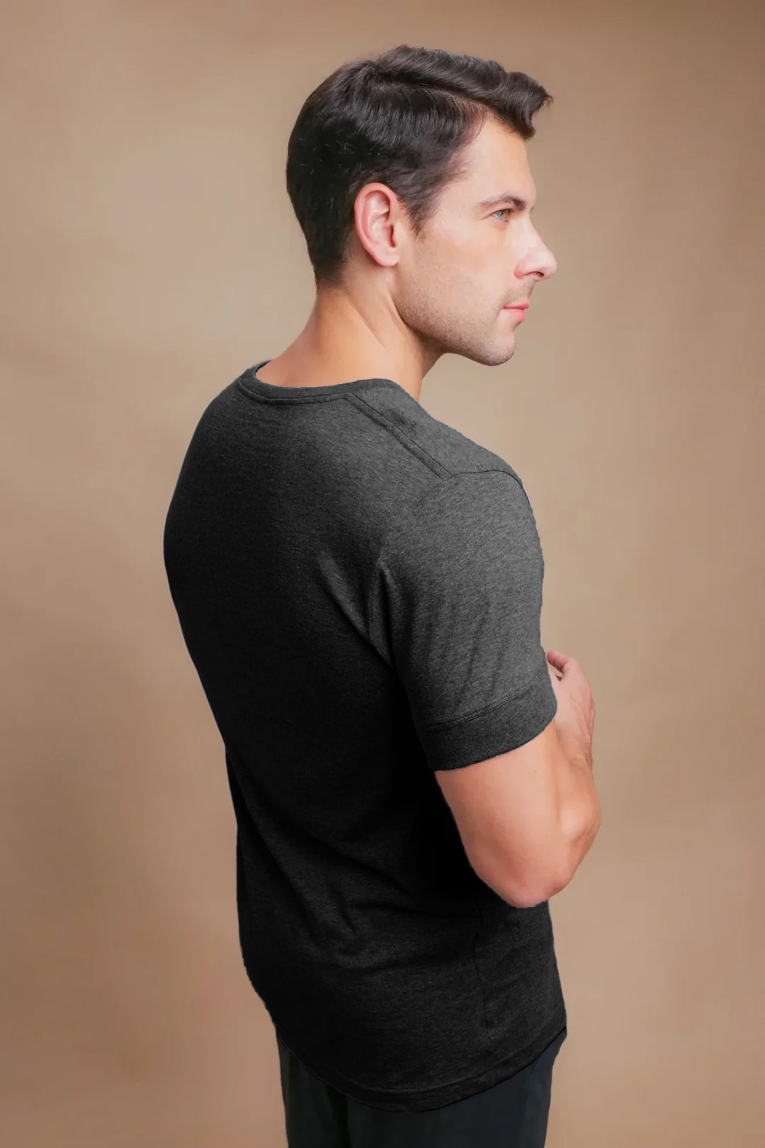 Man wearing dark grey hypoallergenic Cottonique t-shirt, back view, beige background