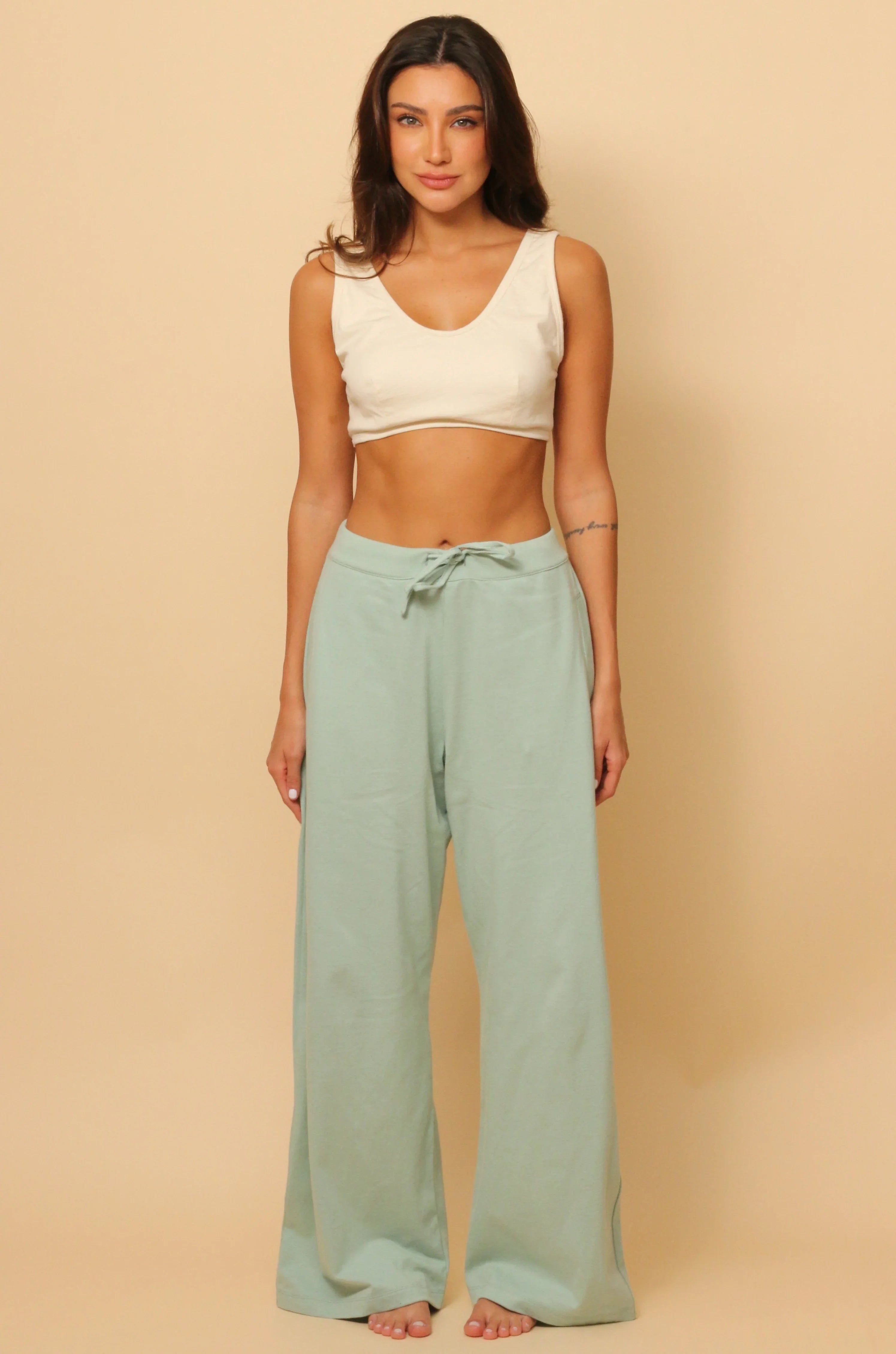 Woman wearing Cottonique hypoallergenic lounge pants and crop top on beige background