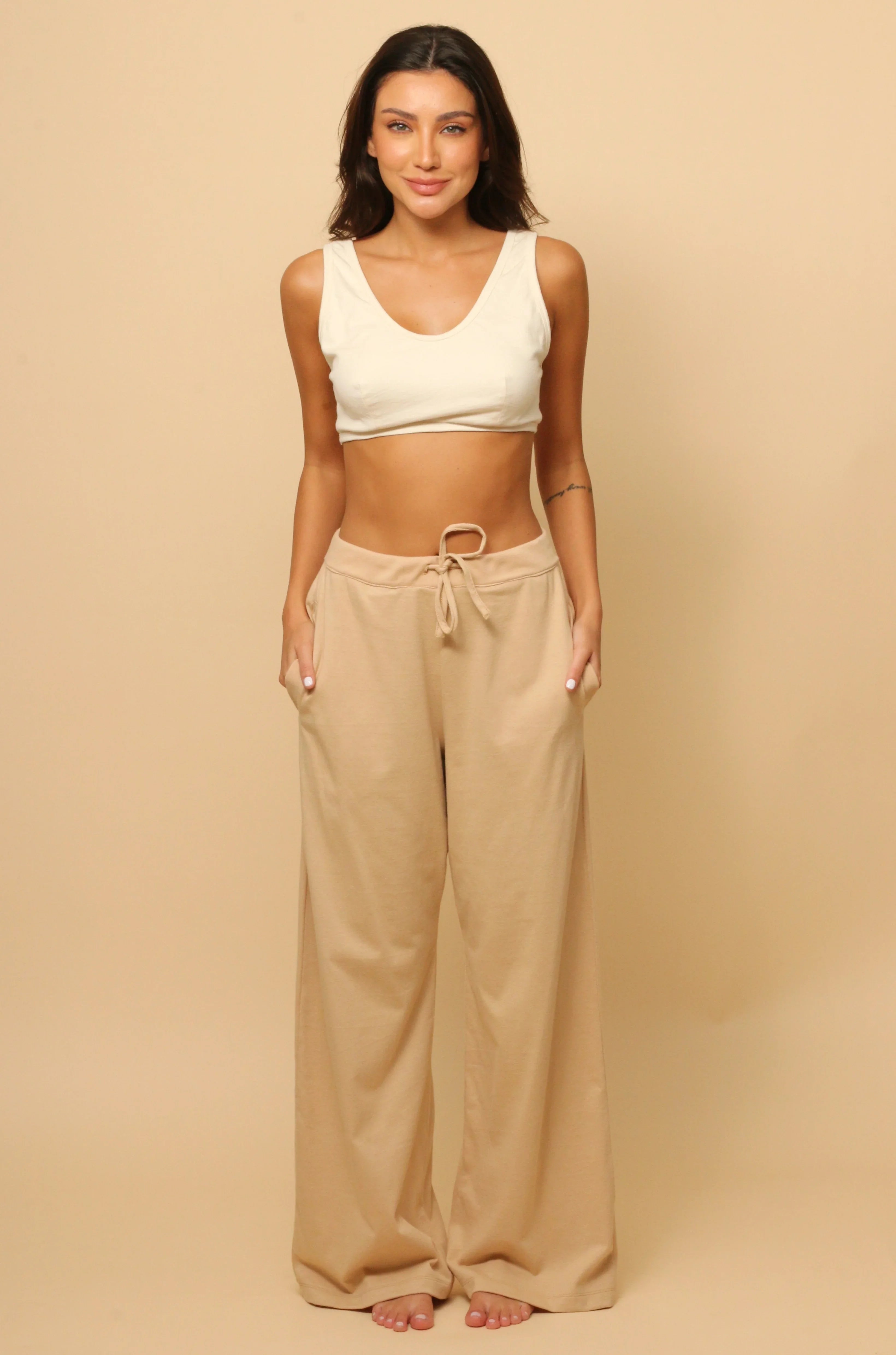 Woman modeling Cottonique hypoallergenic beige lounge pants and cream crop top on beige background