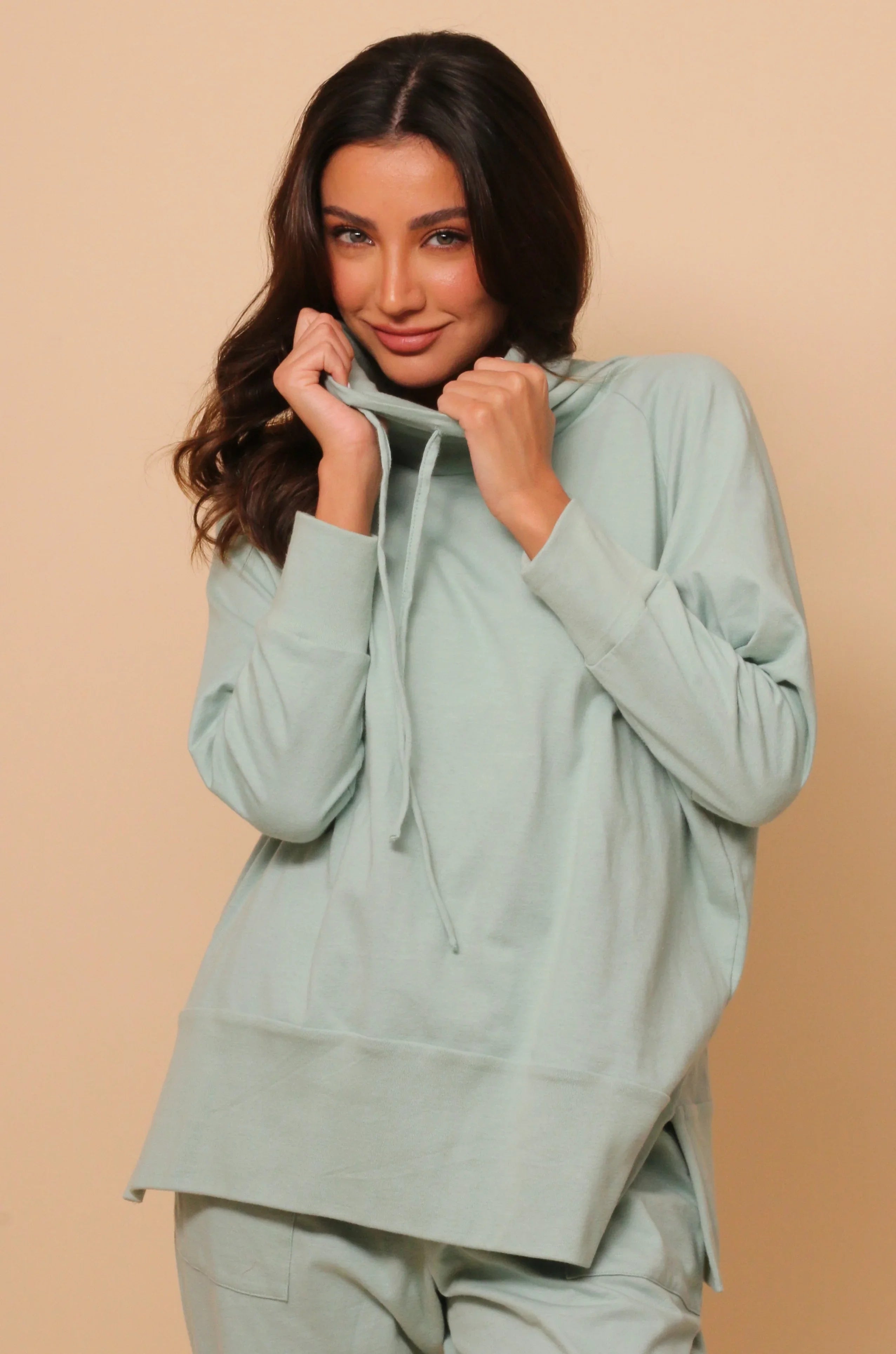 Woman wearing light green hypoallergenic cotton hoodie by Cottonique against beige background
