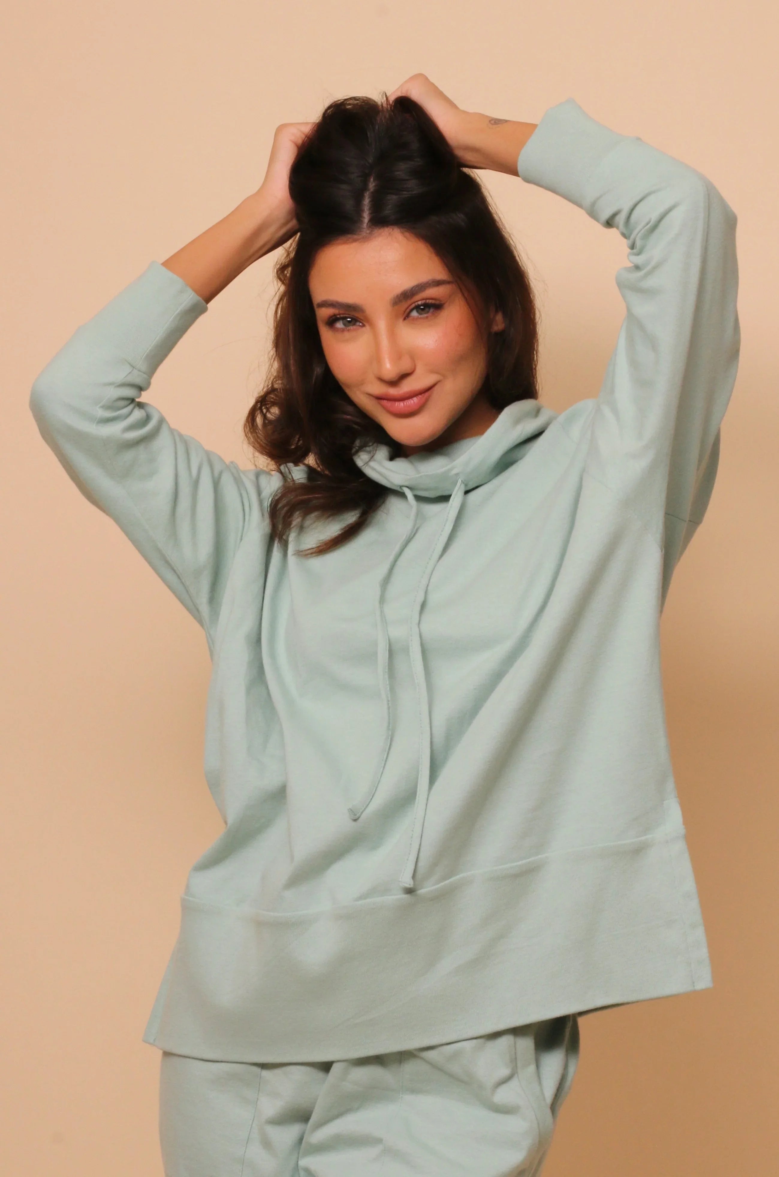 Woman wearing light green hypoallergenic Cottonique hoodie, beige background