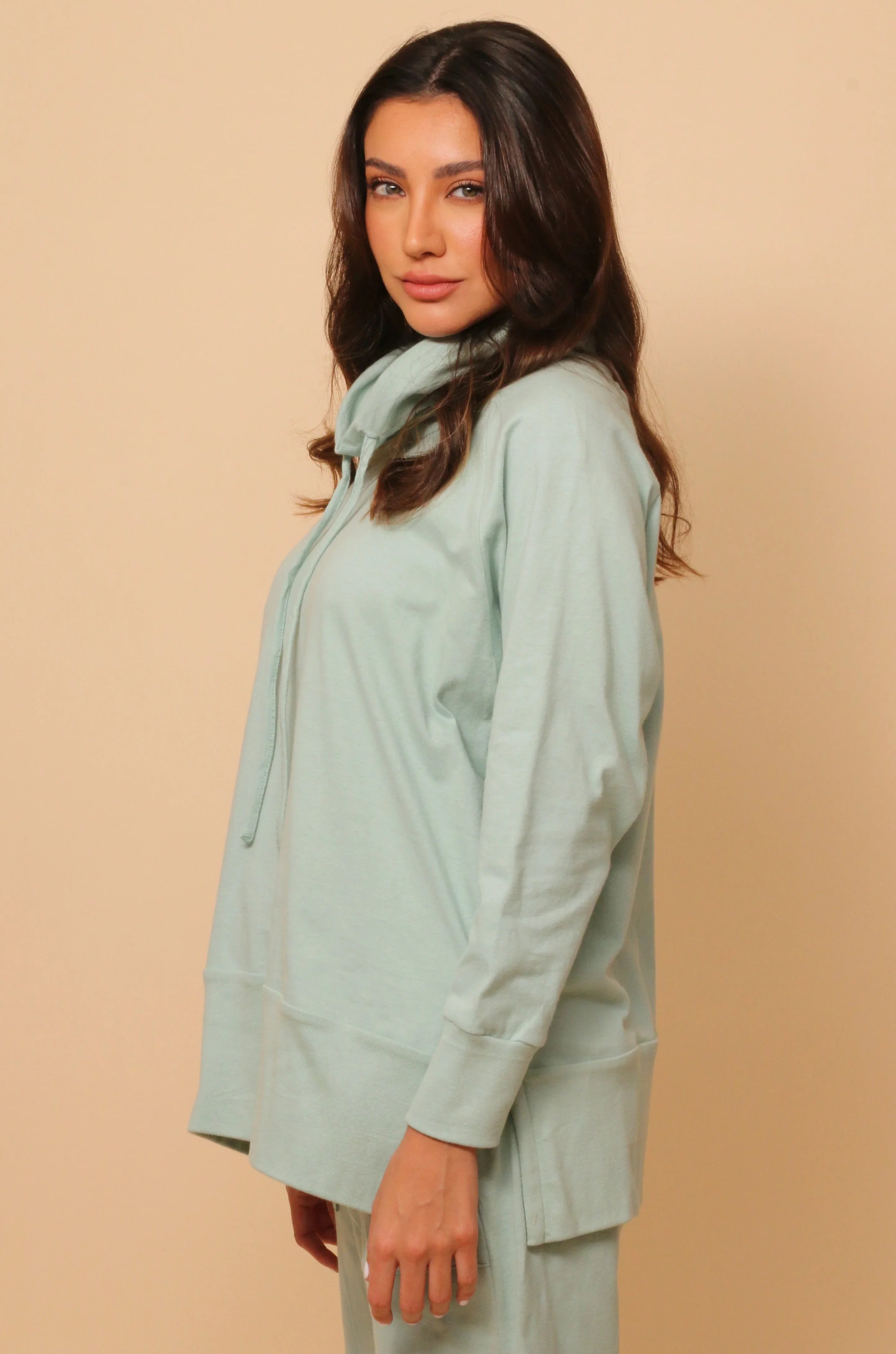 Woman wearing light green hypoallergenic Cottonique sweatshirt and pants, beige background