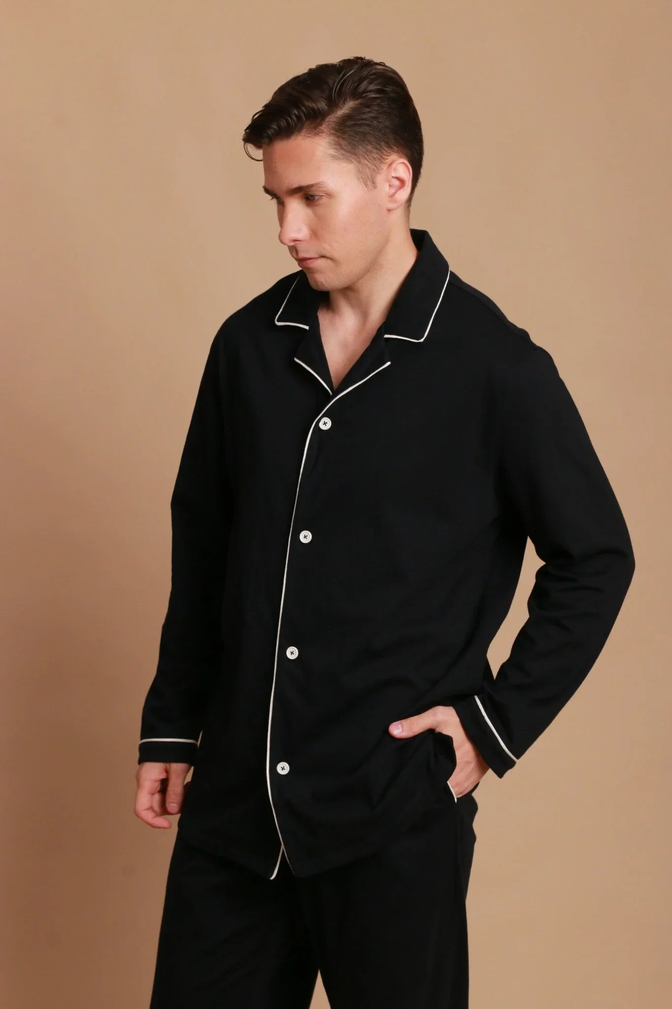 Man wearing black hypoallergenic cotton pajama set from Cottonique, beige background