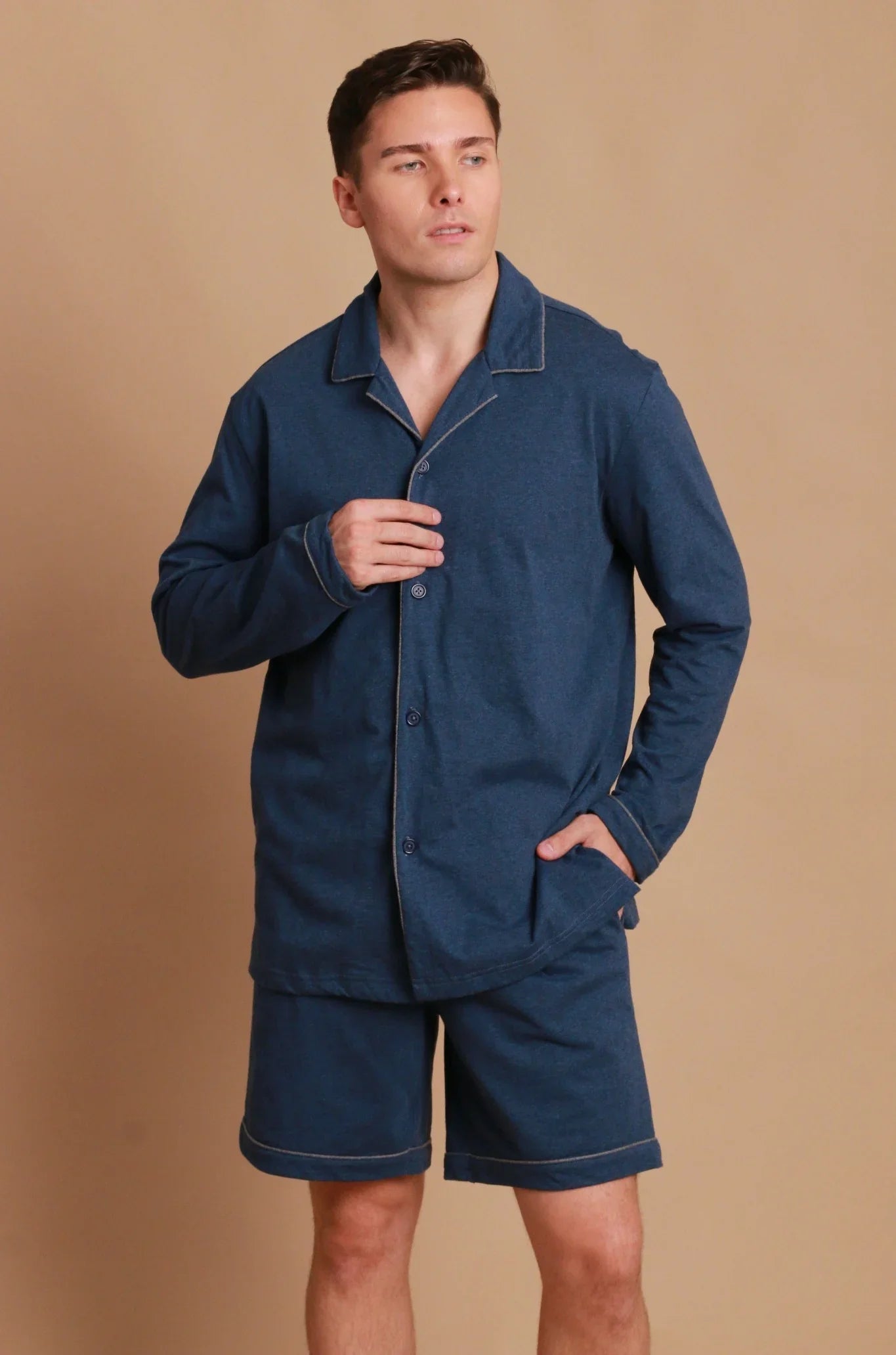 Man wearing blue hypoallergenic cotton pajamas shorts set from Cottonique against tan background