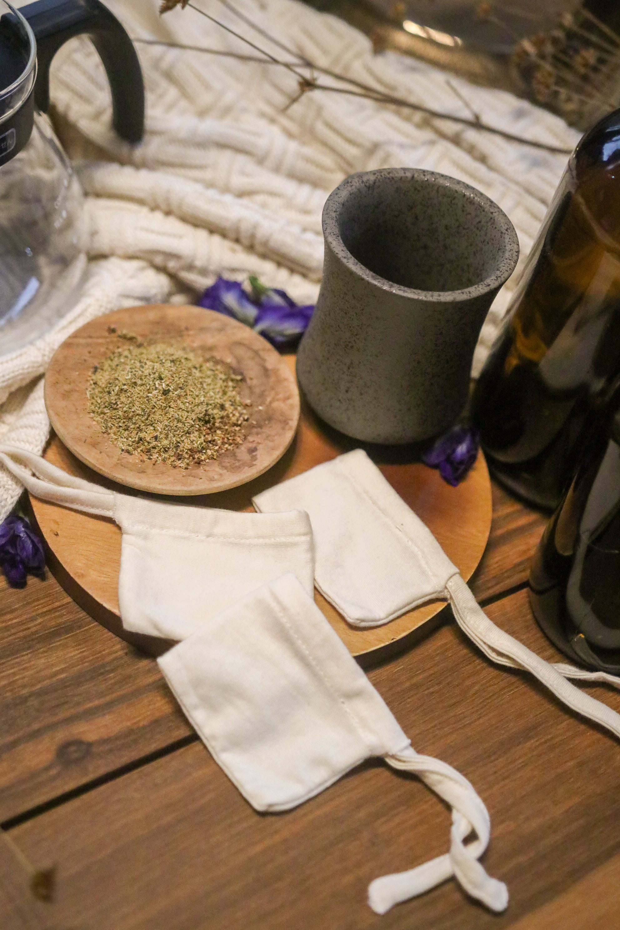 Reusable cotton tea bags beside loose herbal tea and ceramic mug on wooden table, allergy-friendly product.