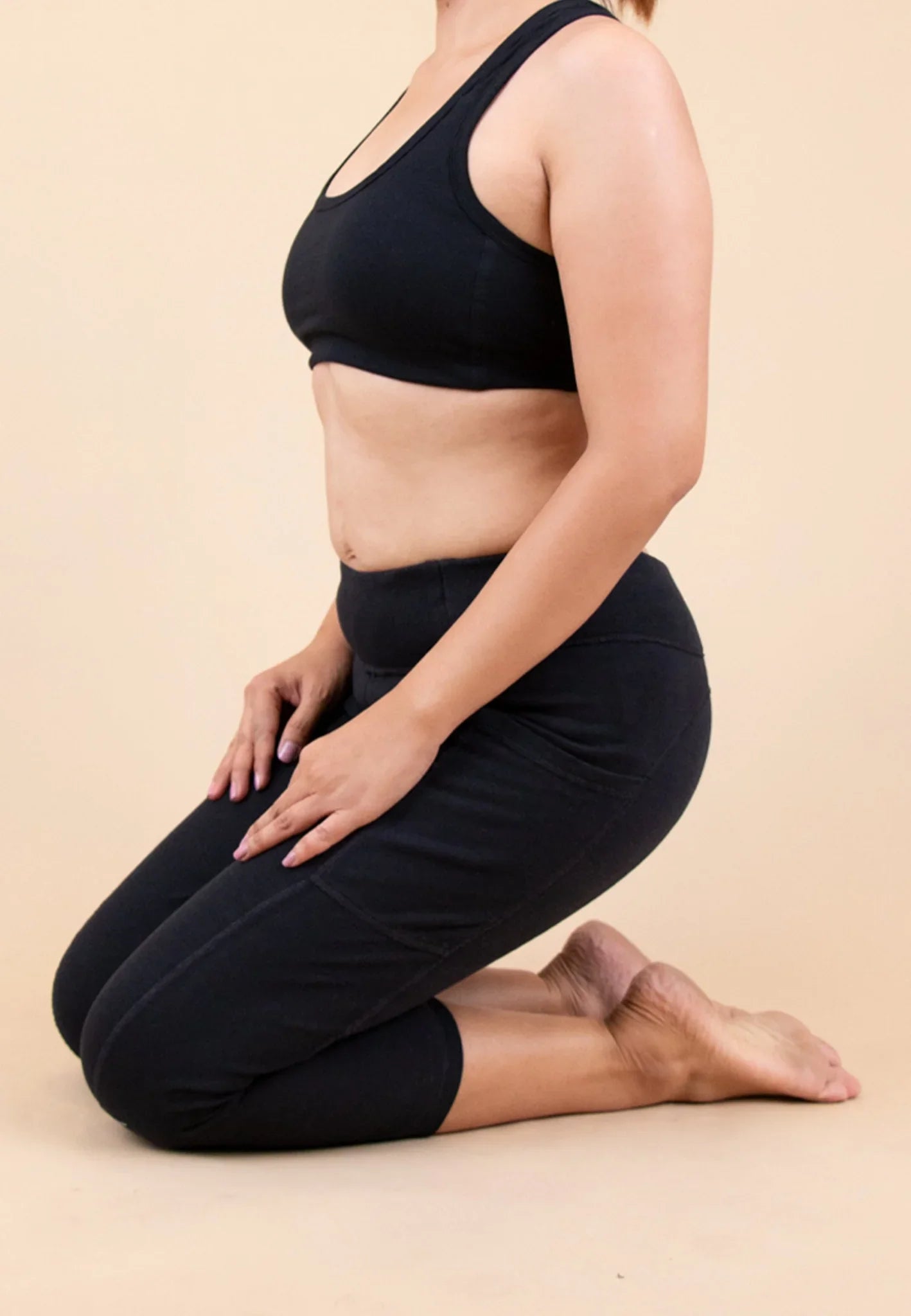 Woman kneeling in black organic cotton allergy-free activewear set on plain background