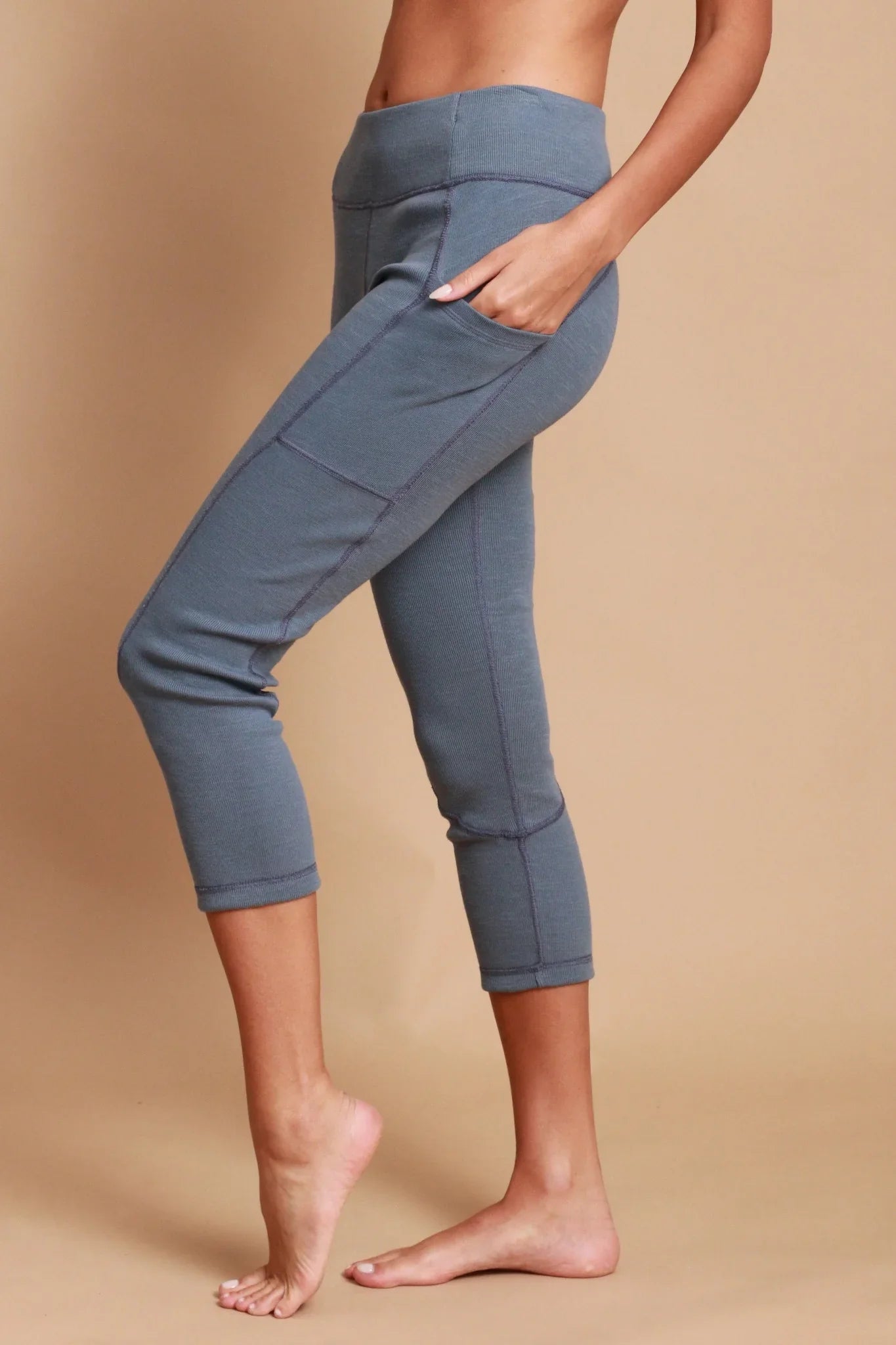 Woman wearing blue hypoallergenic cropped leggings by Cottonique, side view, beige background