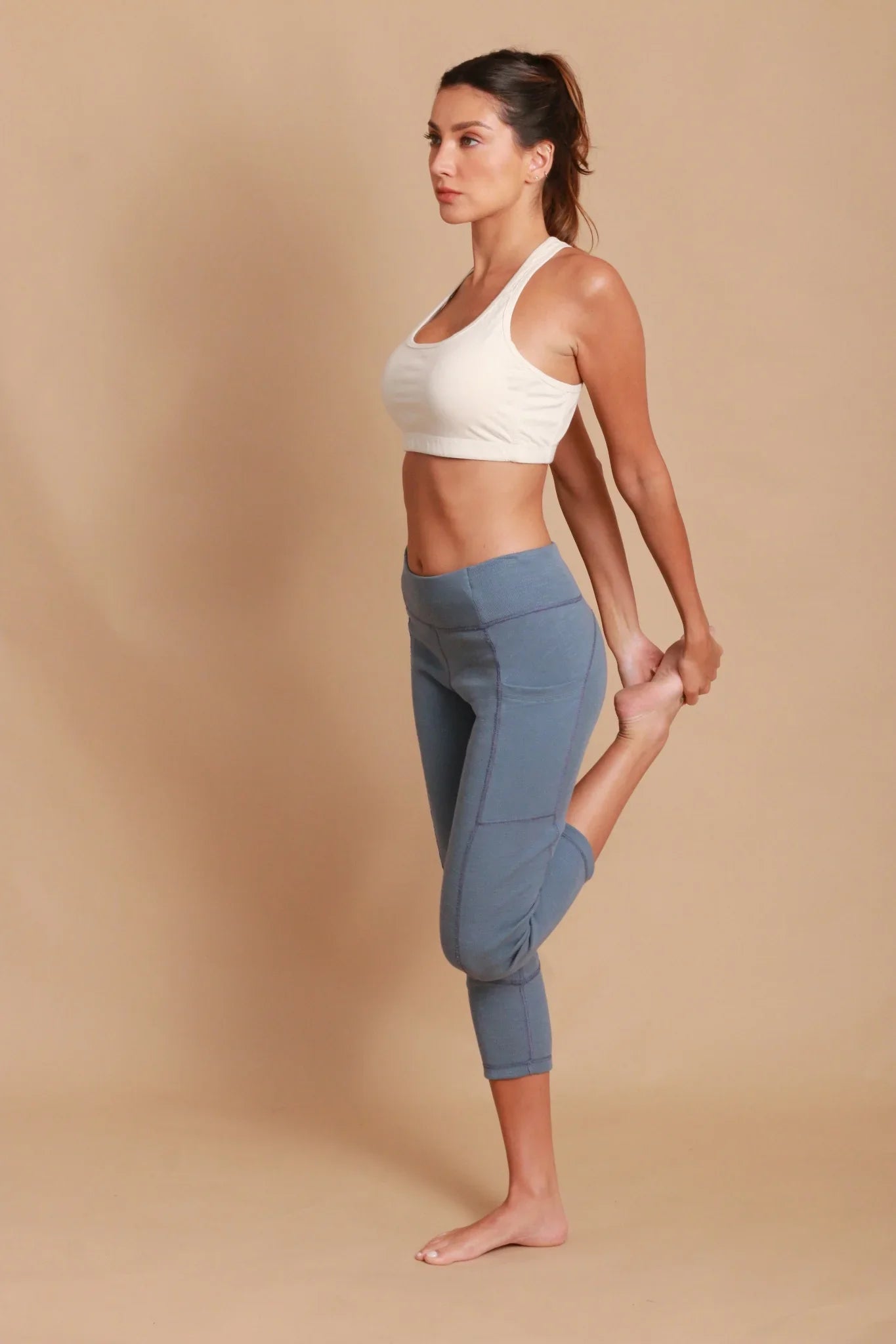 Woman in allergy-free Cottonique sports bra and blue leggings stretching, beige background