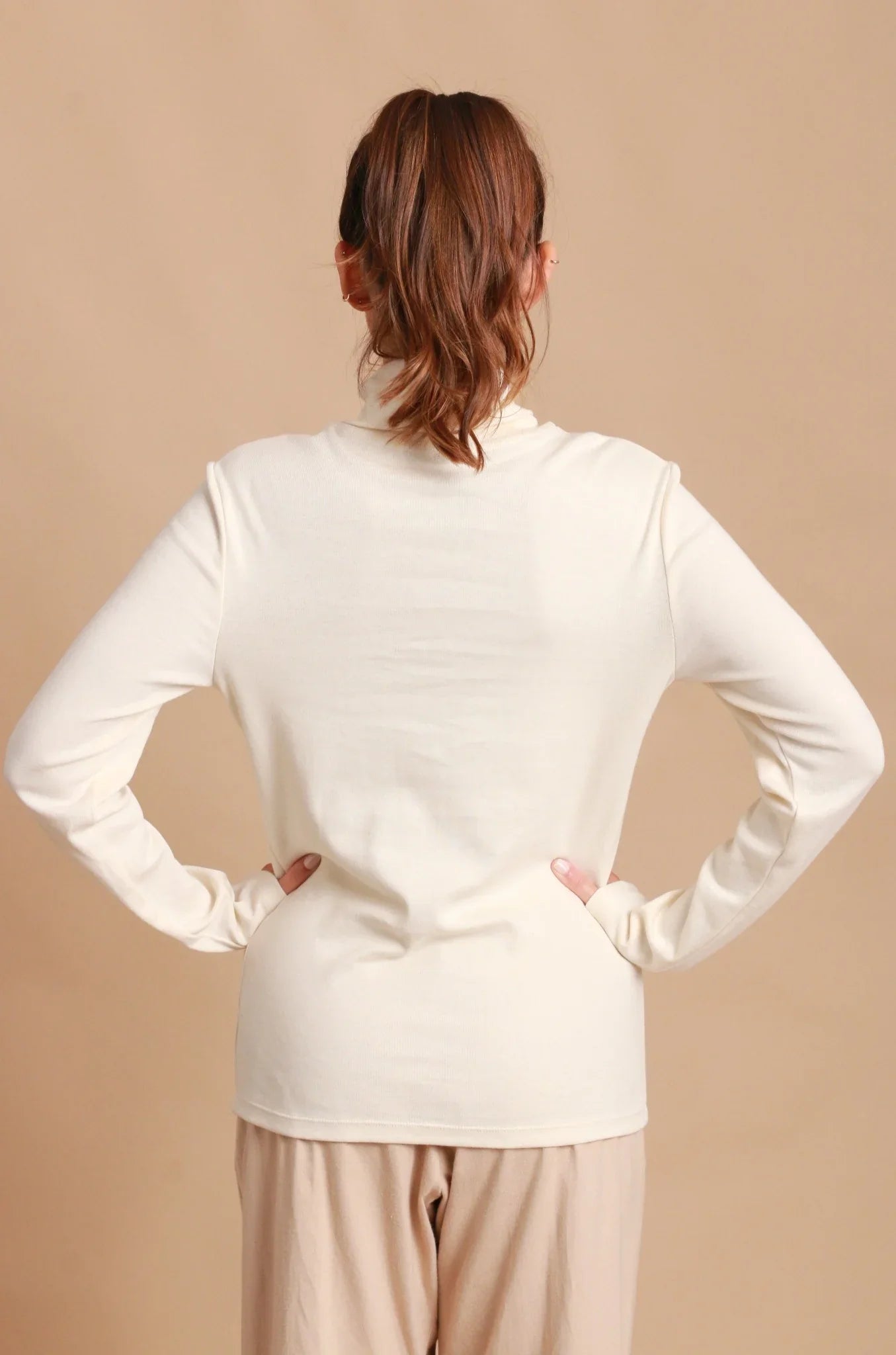 Back view of woman wearing hypoallergenic cream long sleeve Cottonique top and beige pants