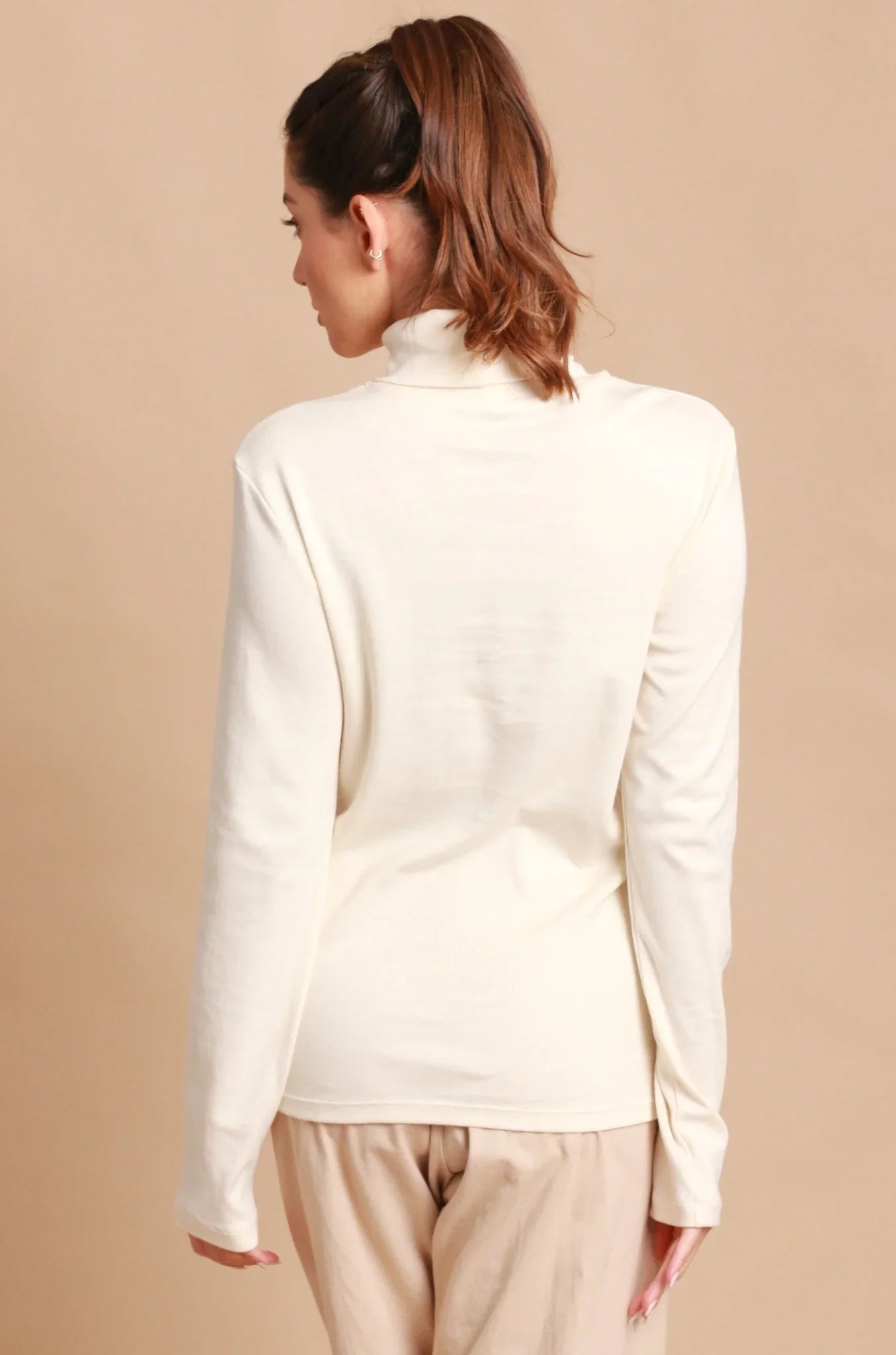 Back view of woman wearing a cream hypoallergenic Cottonique long sleeve turtleneck top