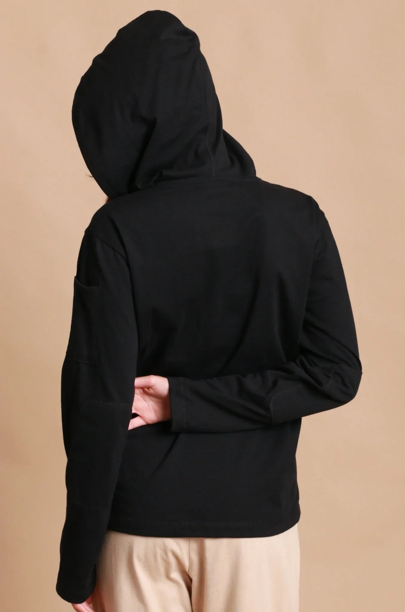 Woman wearing a black organic cotton hoodie with long sleeves, photographed from the back