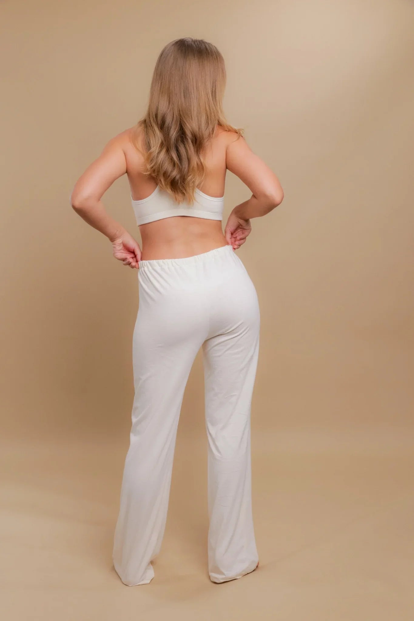 Woman wearing hypoallergenic cotton lounge pants and bra, back view, neutral background.
