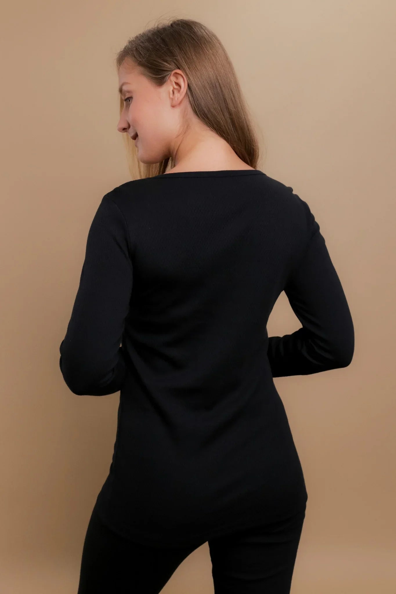 Woman wearing a black long sleeve hypoallergenic Cottonique shirt, back view, beige background