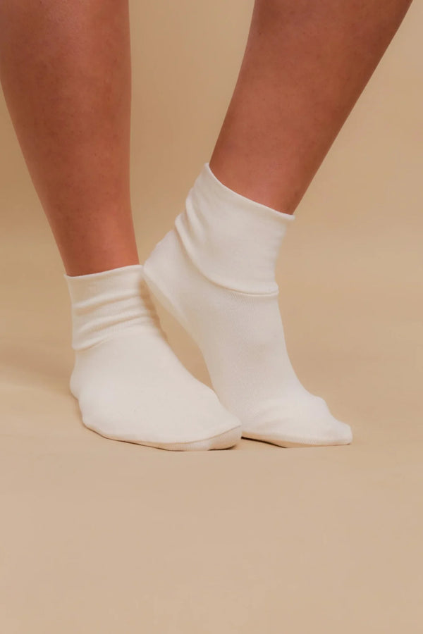 Pair of feet wearing white organic cotton ankle socks for sensitive skin on beige background