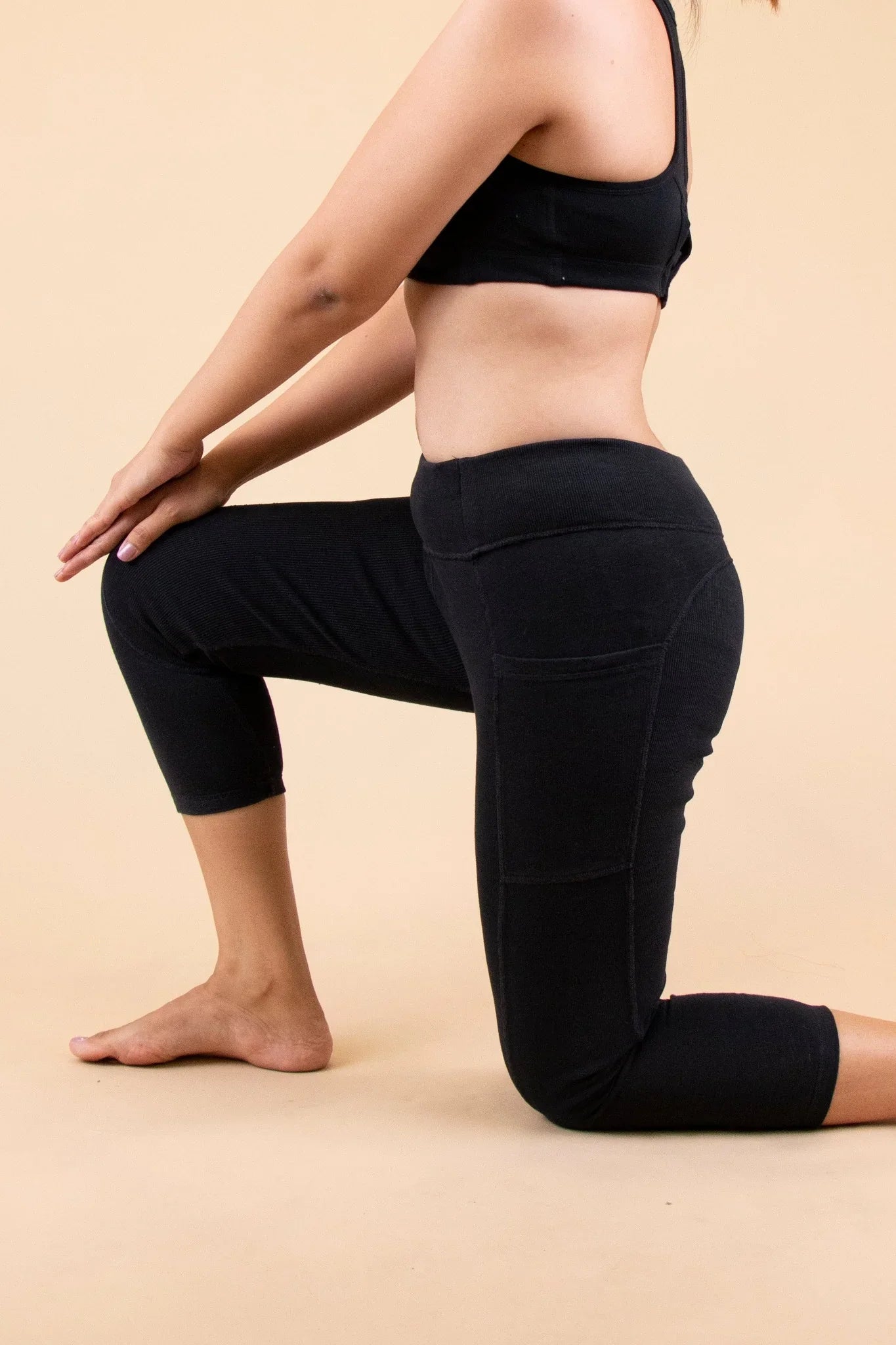 Woman wearing black organic cotton leggings and crop top, kneeling on beige background